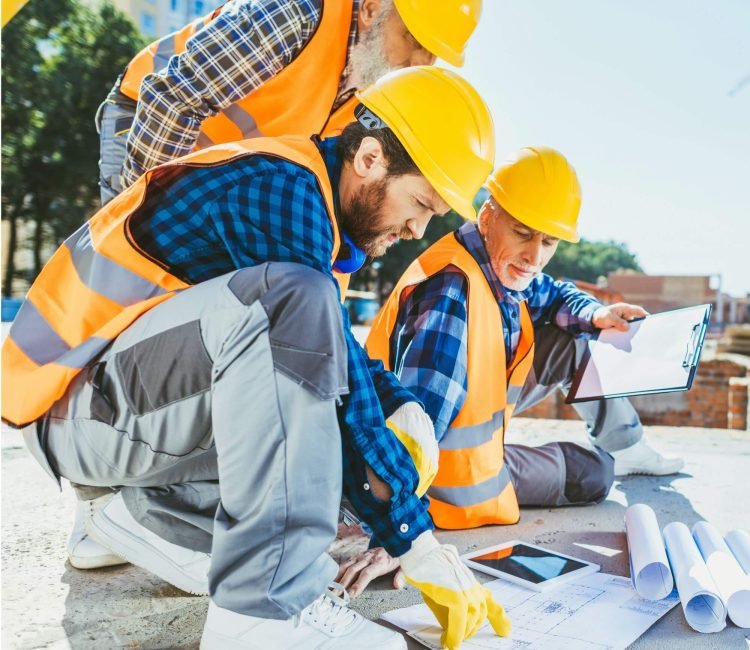 handsome-construction-workers-sitting-on-concrete-at-construction-site-discussing-building-plans-1.jpg
